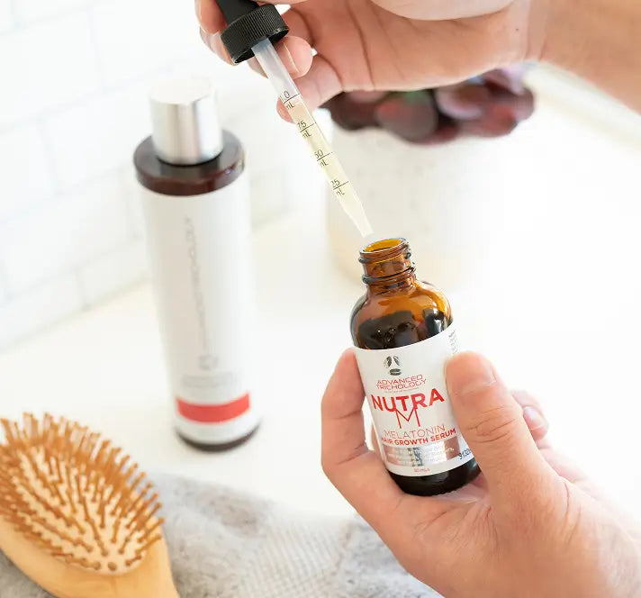 A dropper bottle of Nutra M hair serum held over a bathroom counter