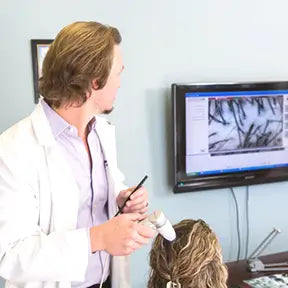 William Gaunitz examining a client’s scalp with a magnified view on screen
